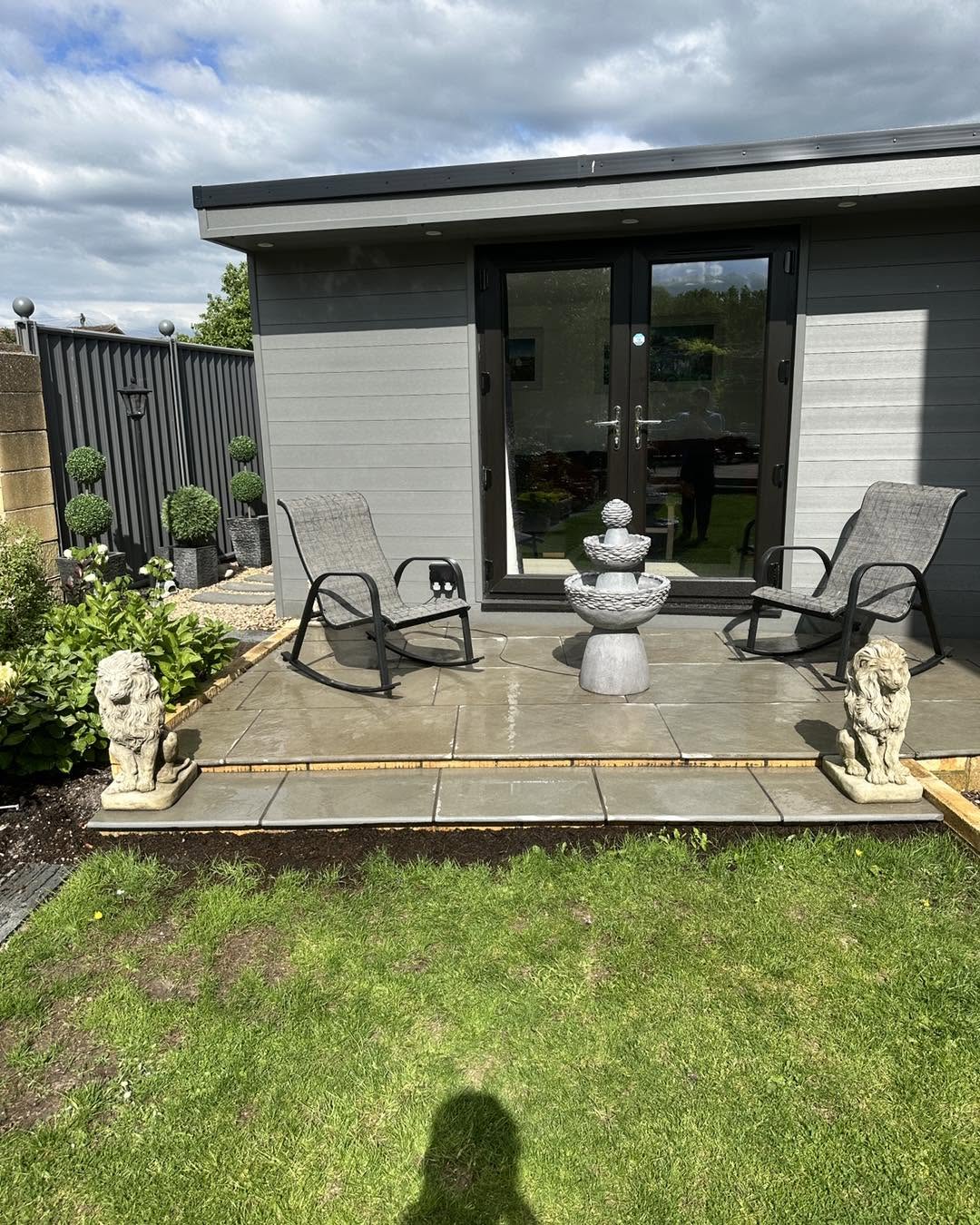 Finished garden with grey garden room, sandstone patio, chairs and a water feature