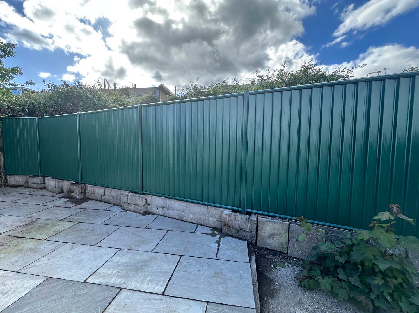Green box-profile metal fence panels above a block base, next to a sandstone patio
