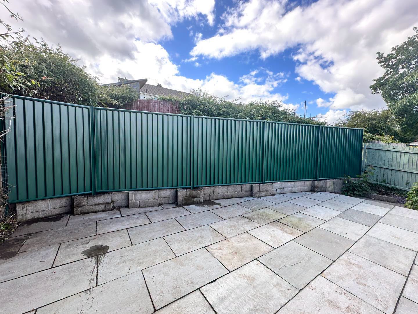 Run of green metal fencing on a low block wall beside a large sandstone patio