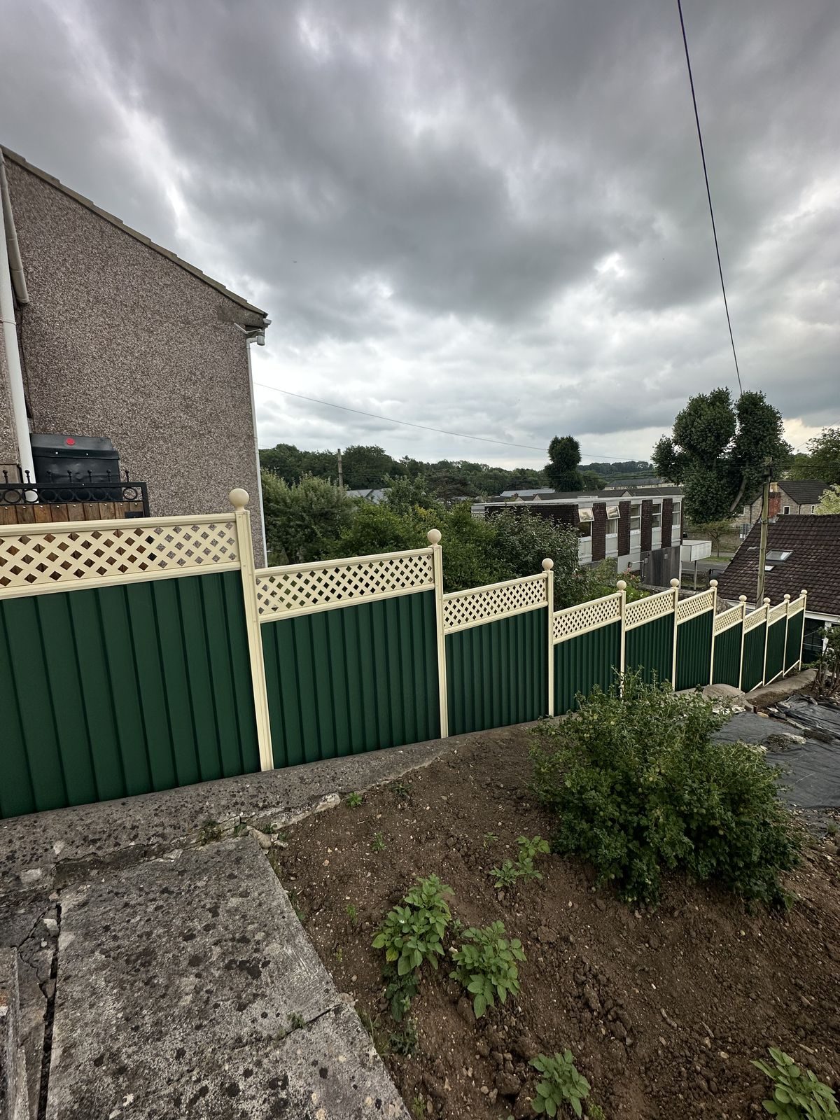 Green metal fencing with cream lattice tops stepping down a sloped boundary overlooking a valley near Bristol