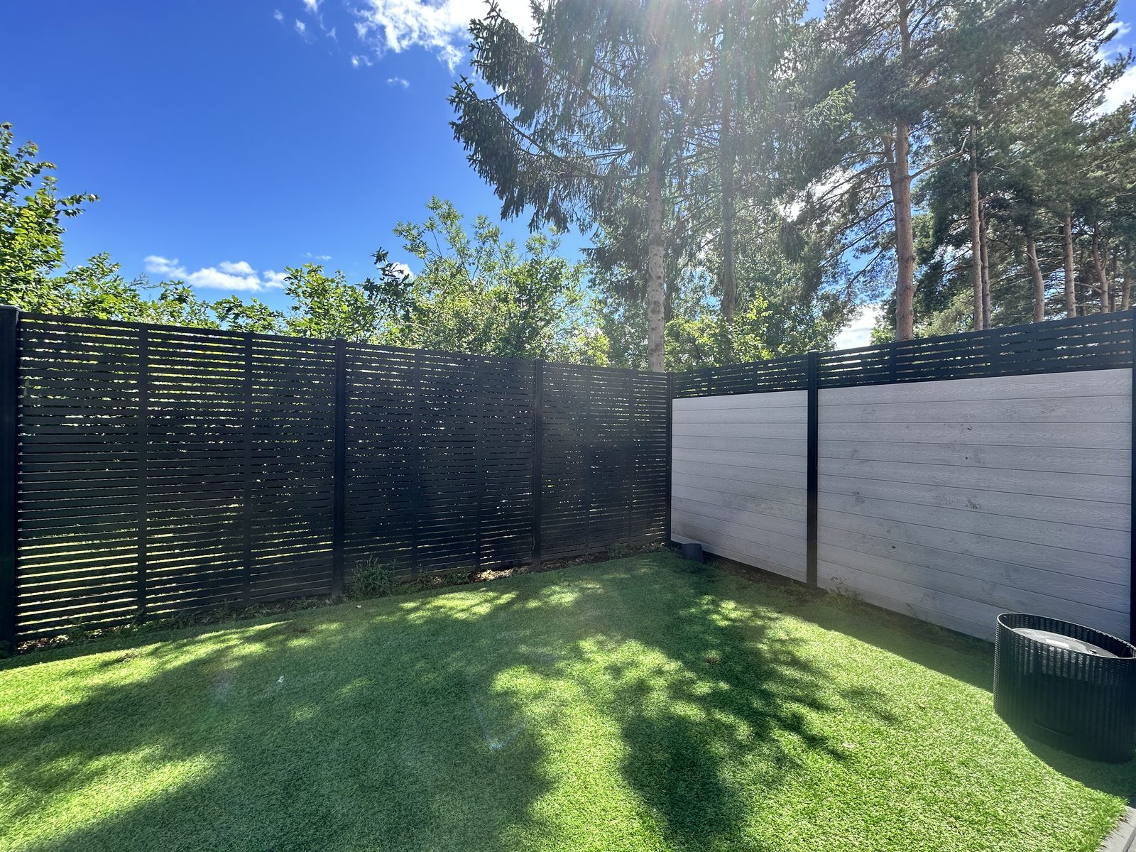 Composite fencing with woodgrain panels and a slatted top around a back garden