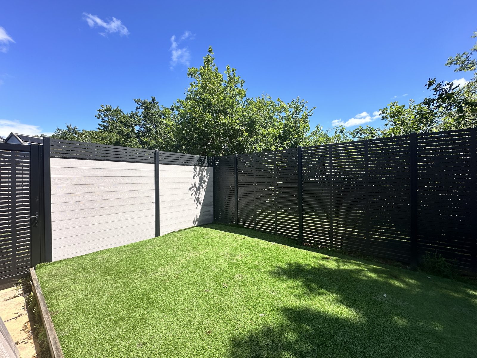 Composite fencing with white woodgrain panels, black posts and a slatted section around a lawn