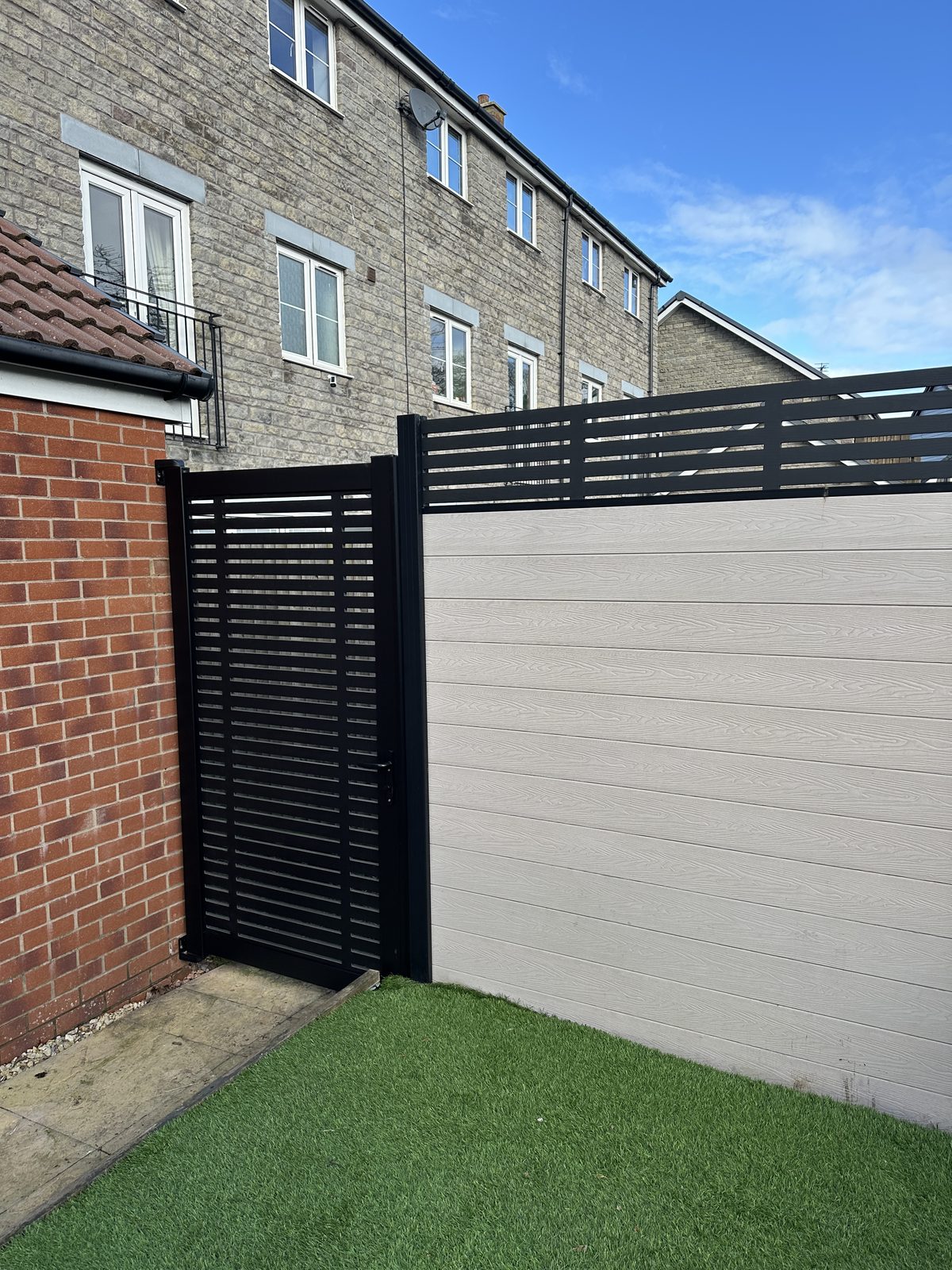 Composite fencing with black slatted and cream woodgrain panels and a matching composite gate down a side return