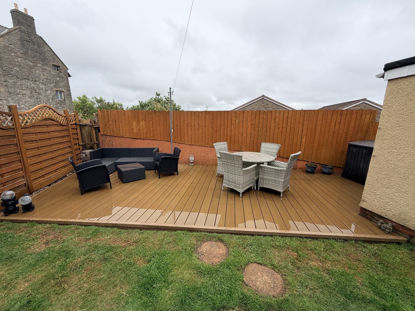 Oak-effect composite decking with rattan seating and a dining set in a back garden