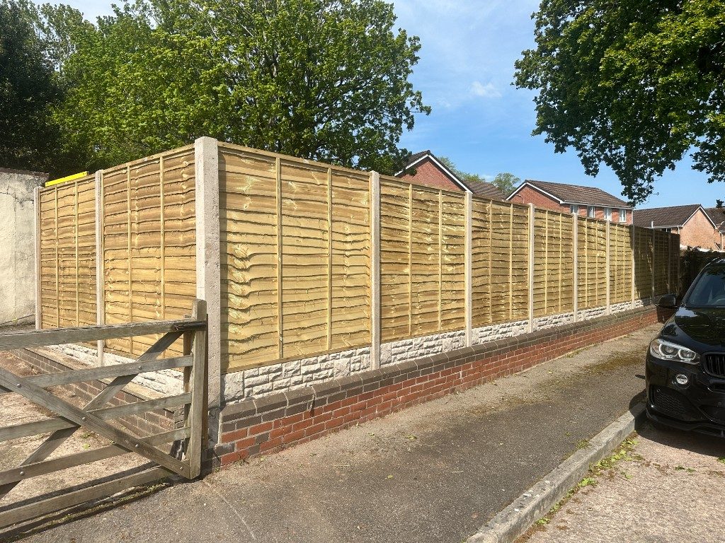 Golden timber featheredge fencing on a stone and brick base along a driveway, beside an old timber gate