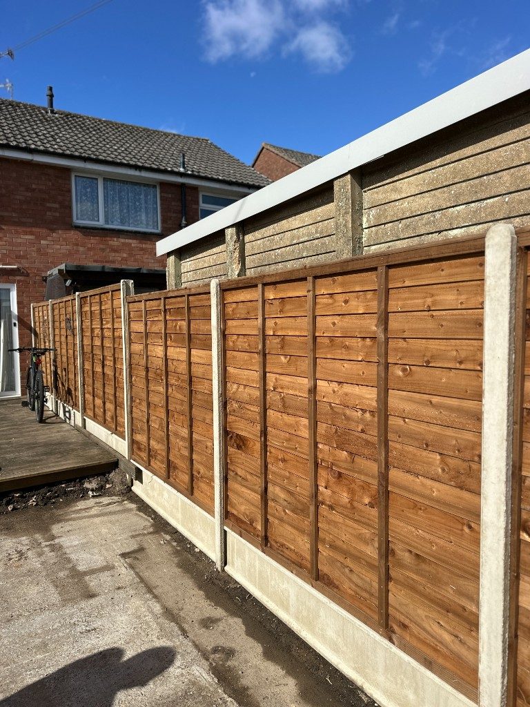 Freshly installed timber featheredge fencing beside a path next to a brick house
