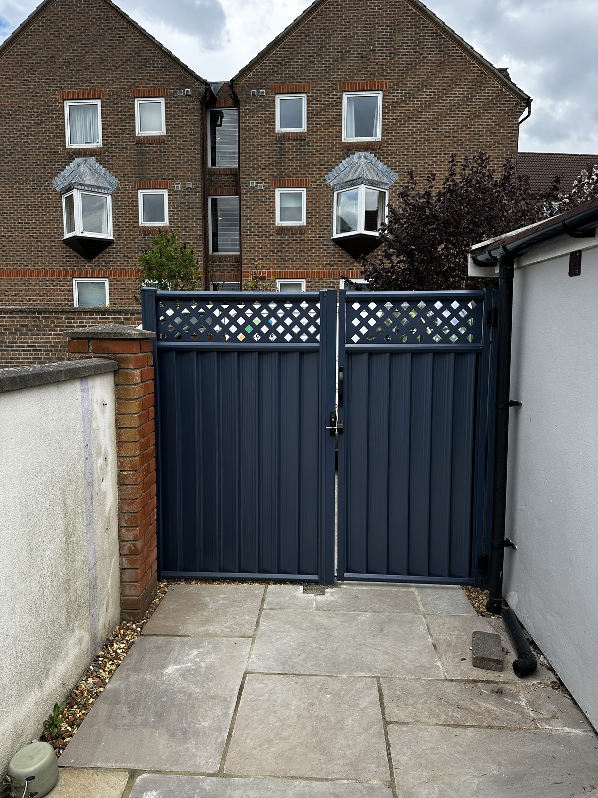 Anthracite grey metal double gates with a lattice top opening onto a paved patio