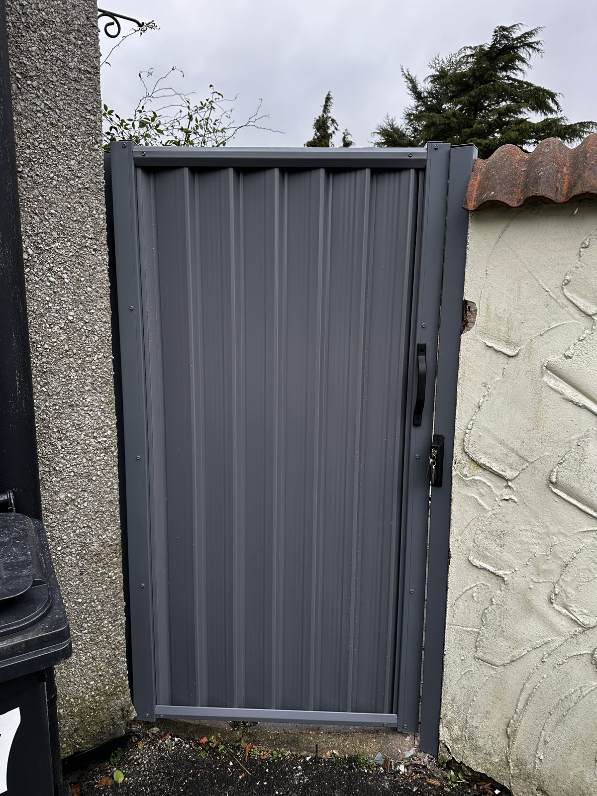 An anthracite grey metal side gate between a rendered wall and a pebbledashed wall