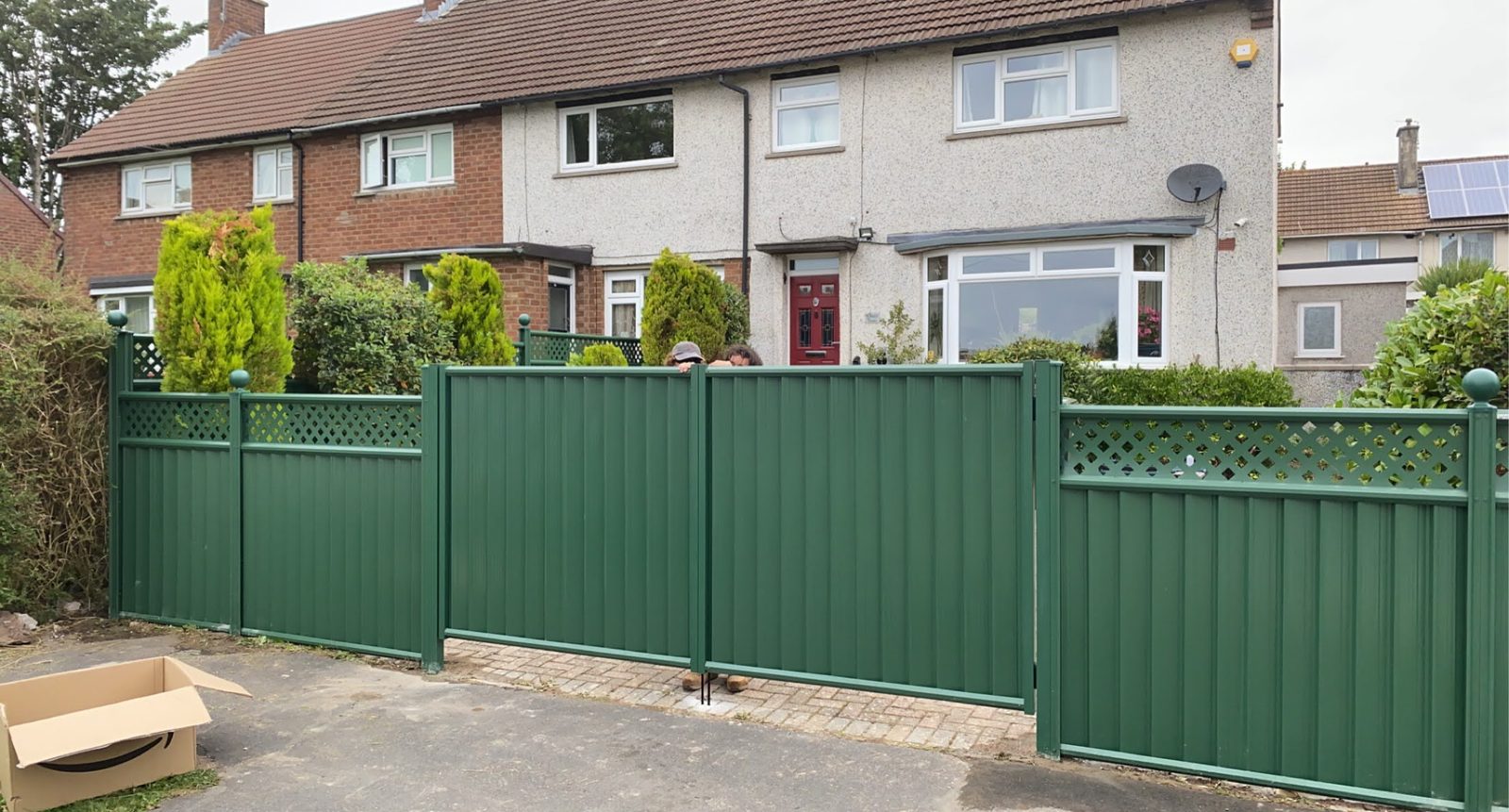 Green metal double driveway gates with matching fencing and a lattice top across a house frontage