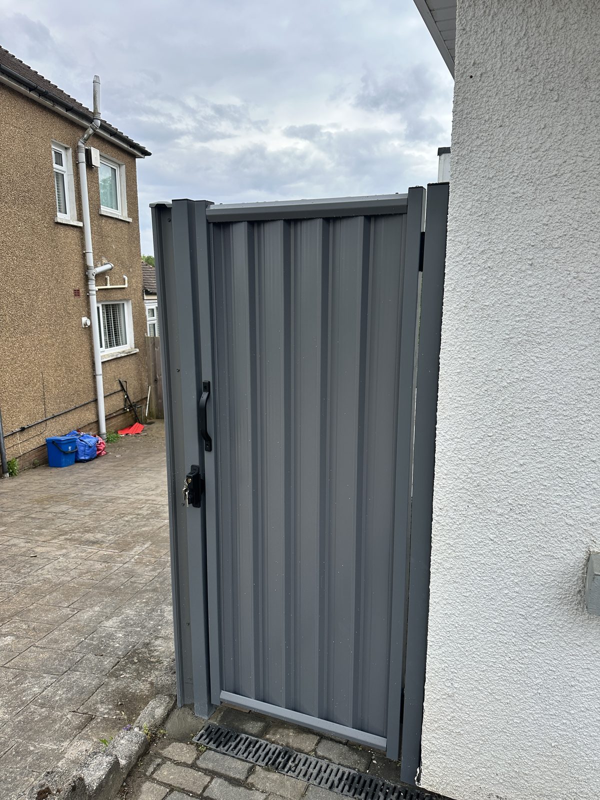 A grey metal side gate fitted between a house and boundary wall