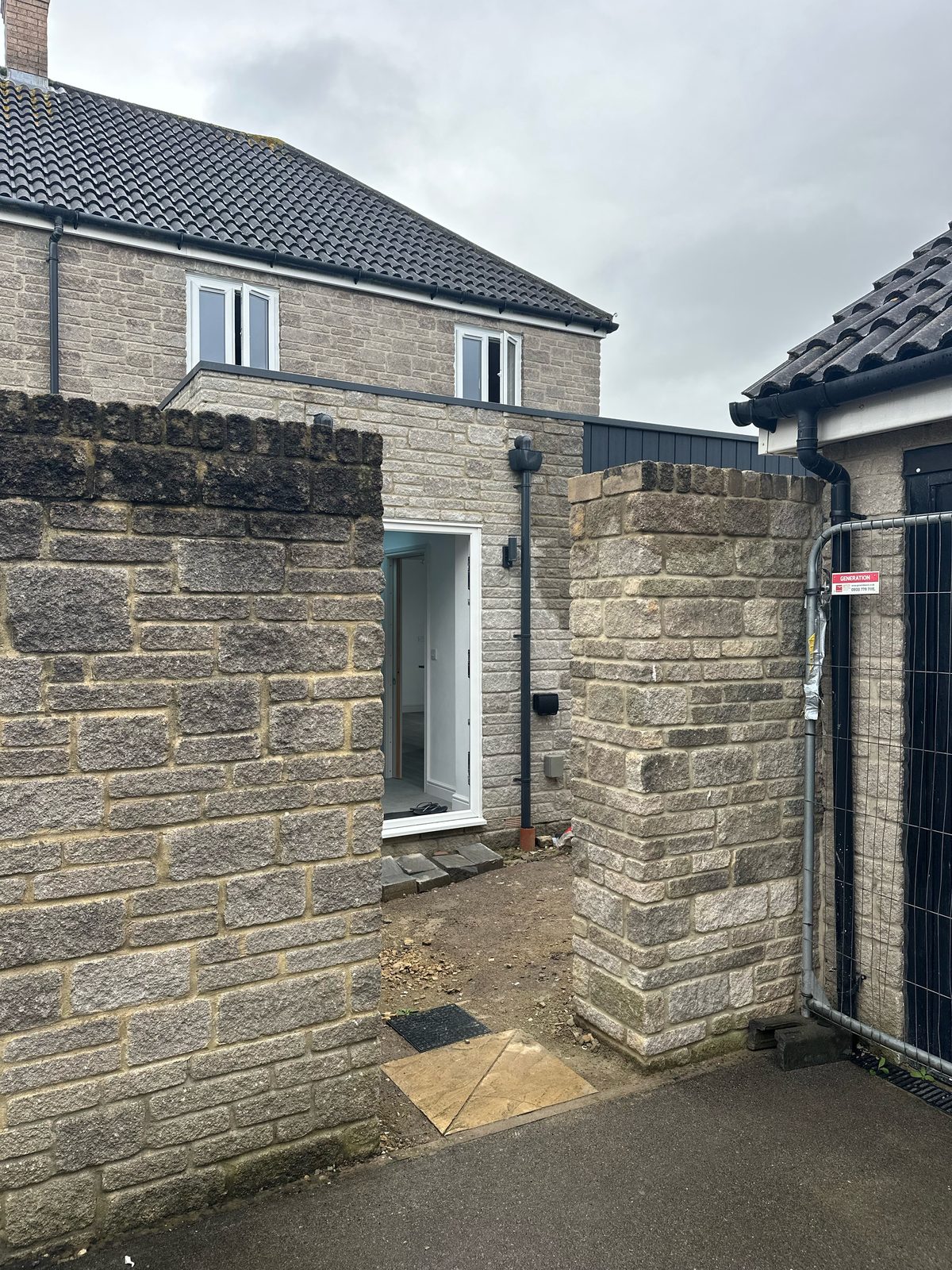 Before: an open gap between stone wall pillars with no gate, fenced off temporarily