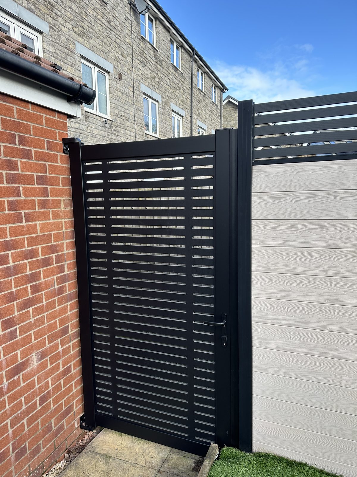 A black aluminium slatted side gate fitted alongside composite fencing with a slatted top