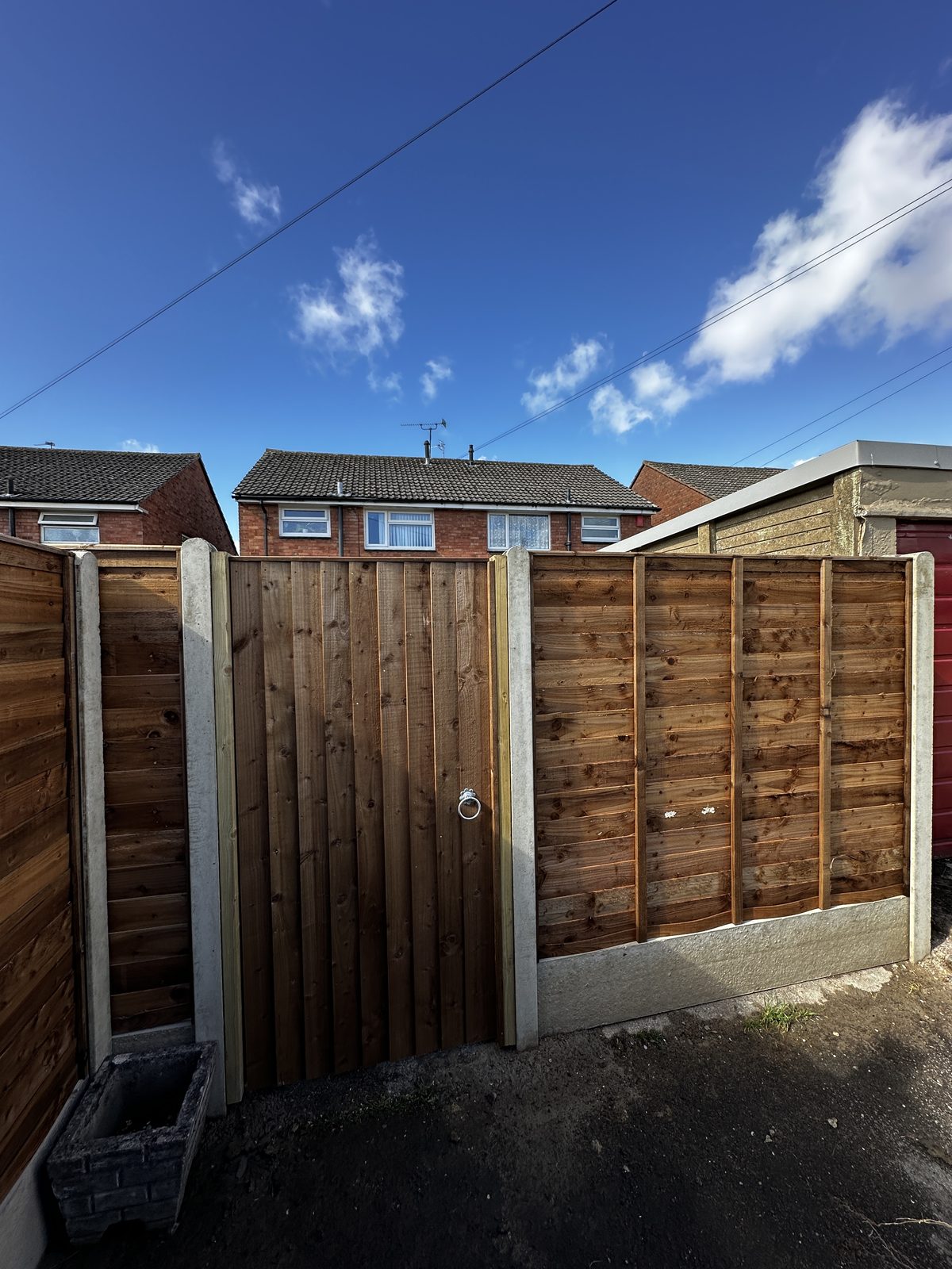 A timber featheredge side gate with a ring latch between concrete-post fence panels