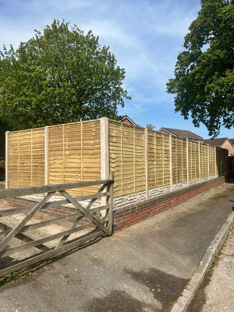 A run of timber featheredge fencing on a stone and brick base along a driveway