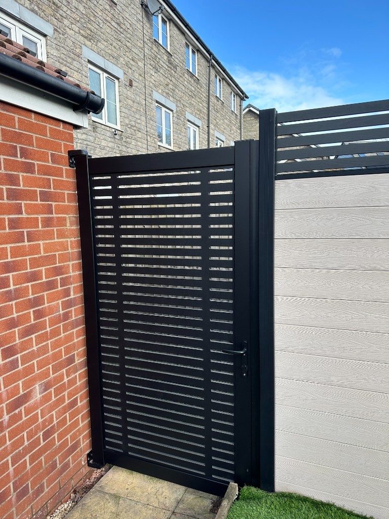 A black aluminium slatted side gate fitted alongside grey composite fencing
