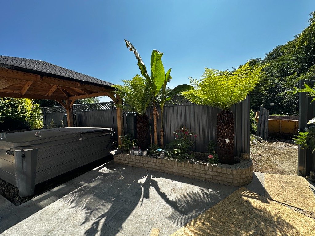 A finished garden with porcelain patio, raised planting beds, palms and a hot tub under a gazebo