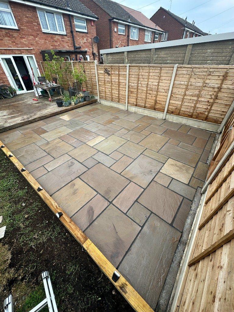 A riven Indian sandstone patio with dark jointing and timber edging beside a deck