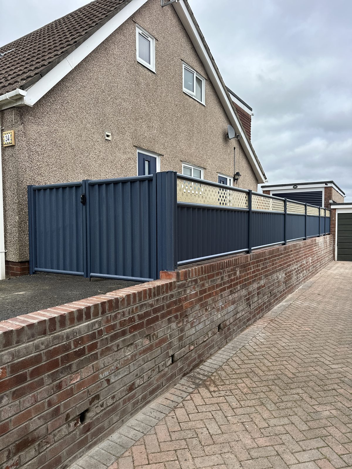 Navy metal fencing manufactured from Colorbond steel with a matching gate and slatted-top accent along a block-paved drive