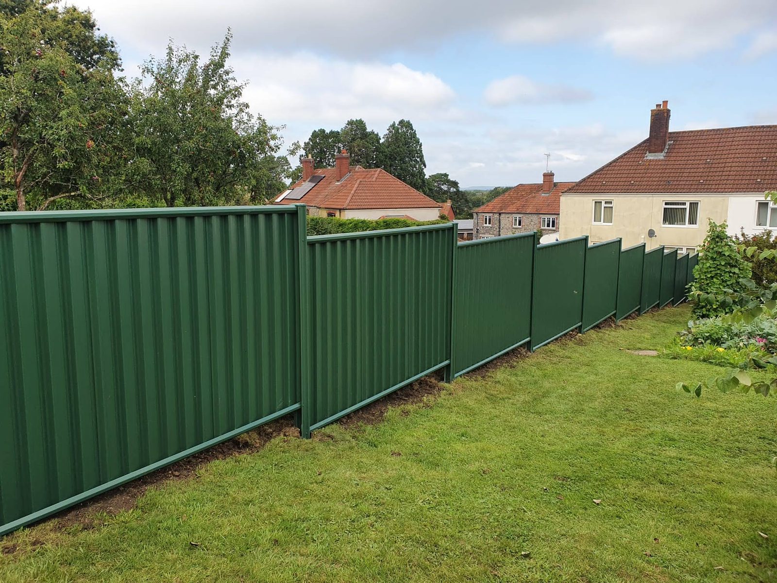 Green metal fencing running along a back garden lawn
