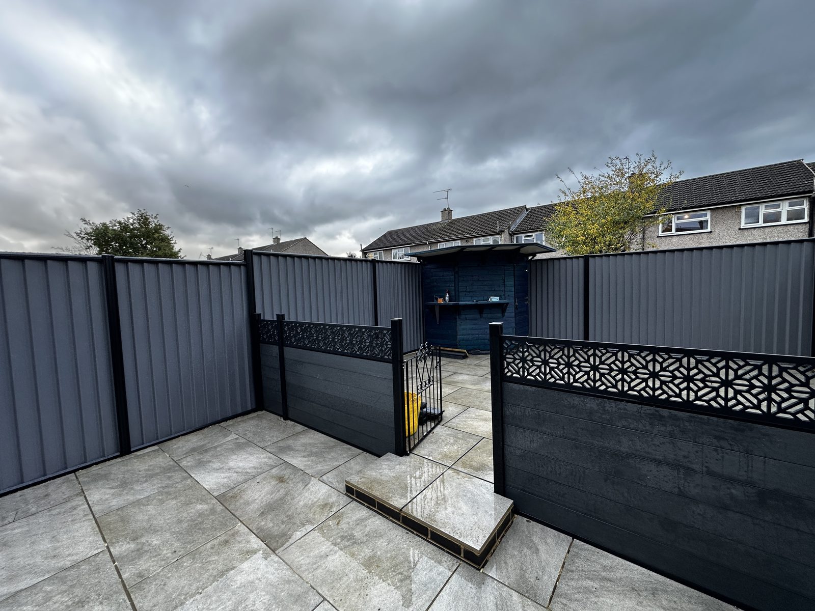 Anthracite metal fencing and a navy gate around a sandstone patio