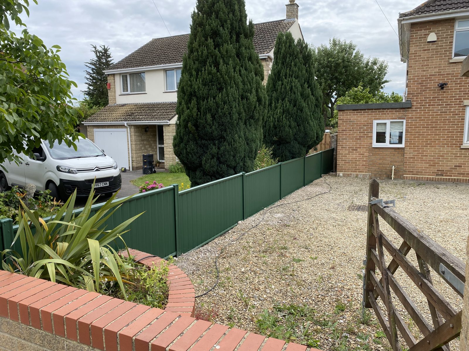 Green metal fencing with a matching timber gate beside a driveway