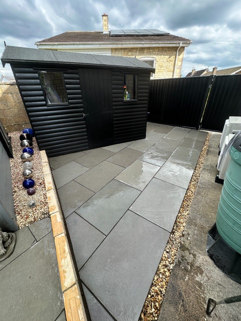 After: smart grey porcelain paving laid beside the shed with a gravel border