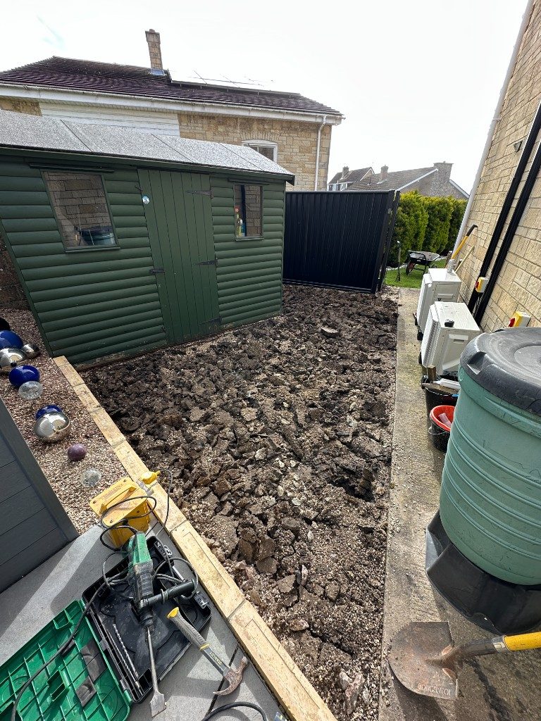 Before: ground broken up and dug out alongside a shed, ready for a new patio