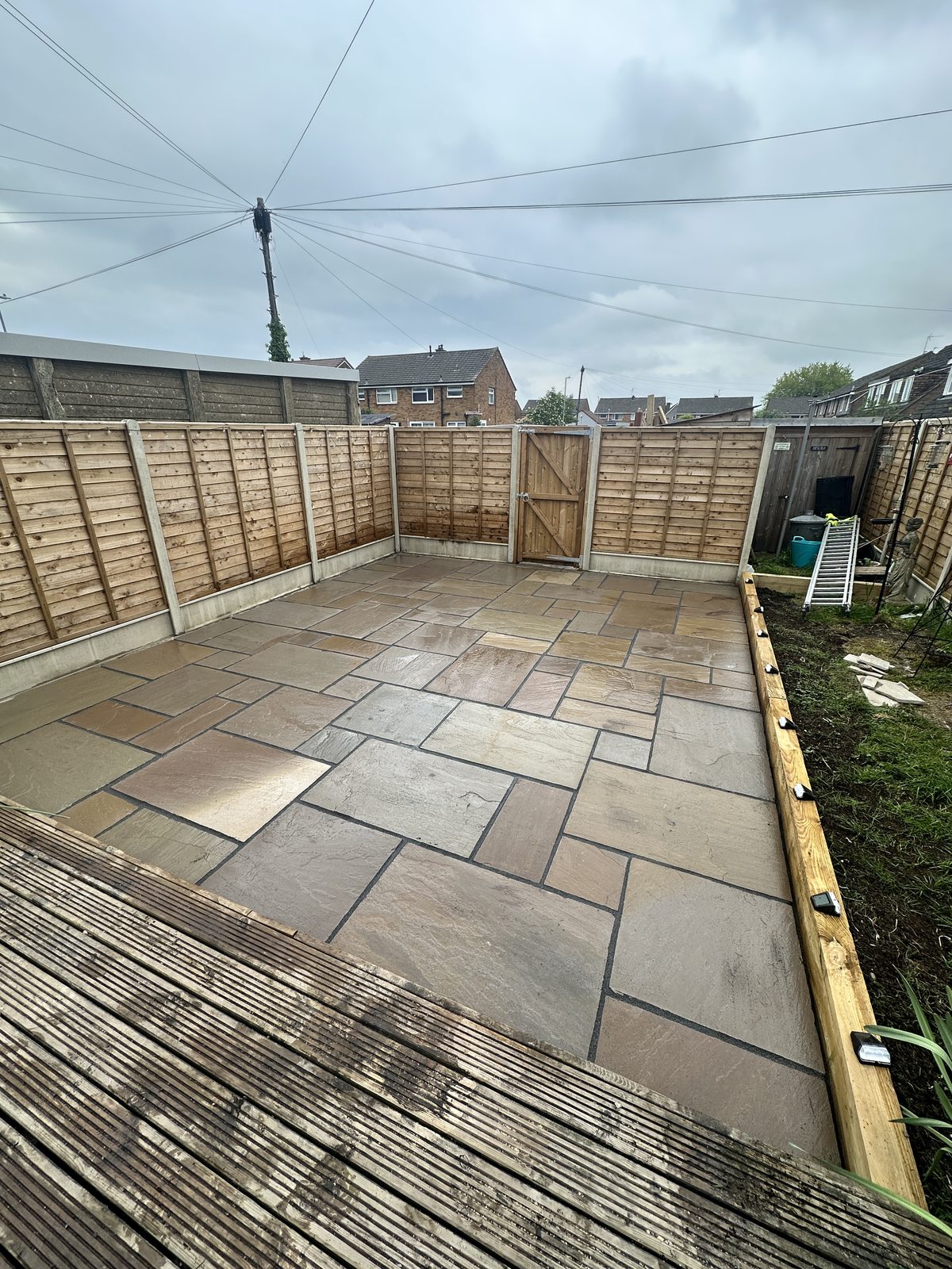 Indian sandstone patio with riven slabs beside a timber fence and brick house