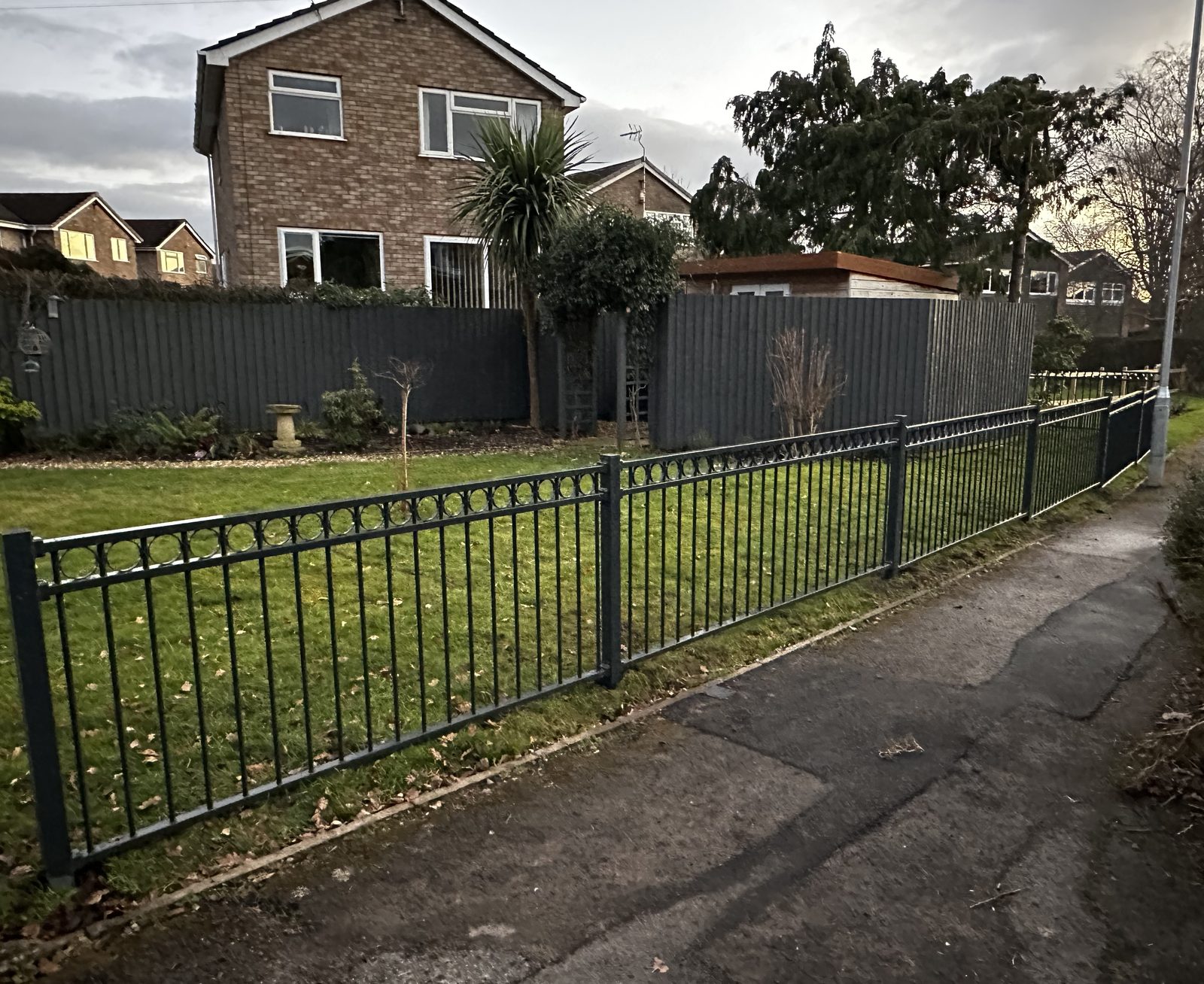 Black metal railings enclosing a front garden by a brick house