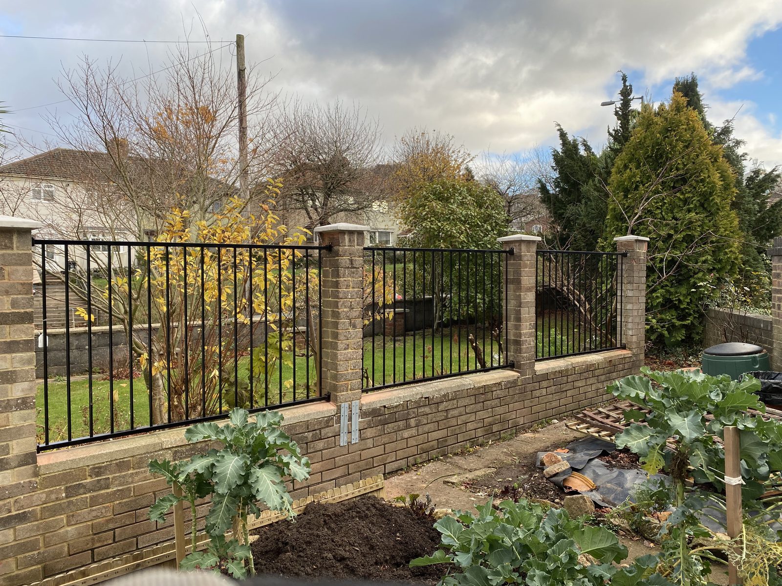 Black metal railings on brick pillars along a garden boundary