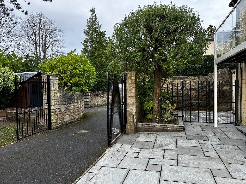 Black metal railings and matching gates beside a stone wall, alongside a grey sandstone patio