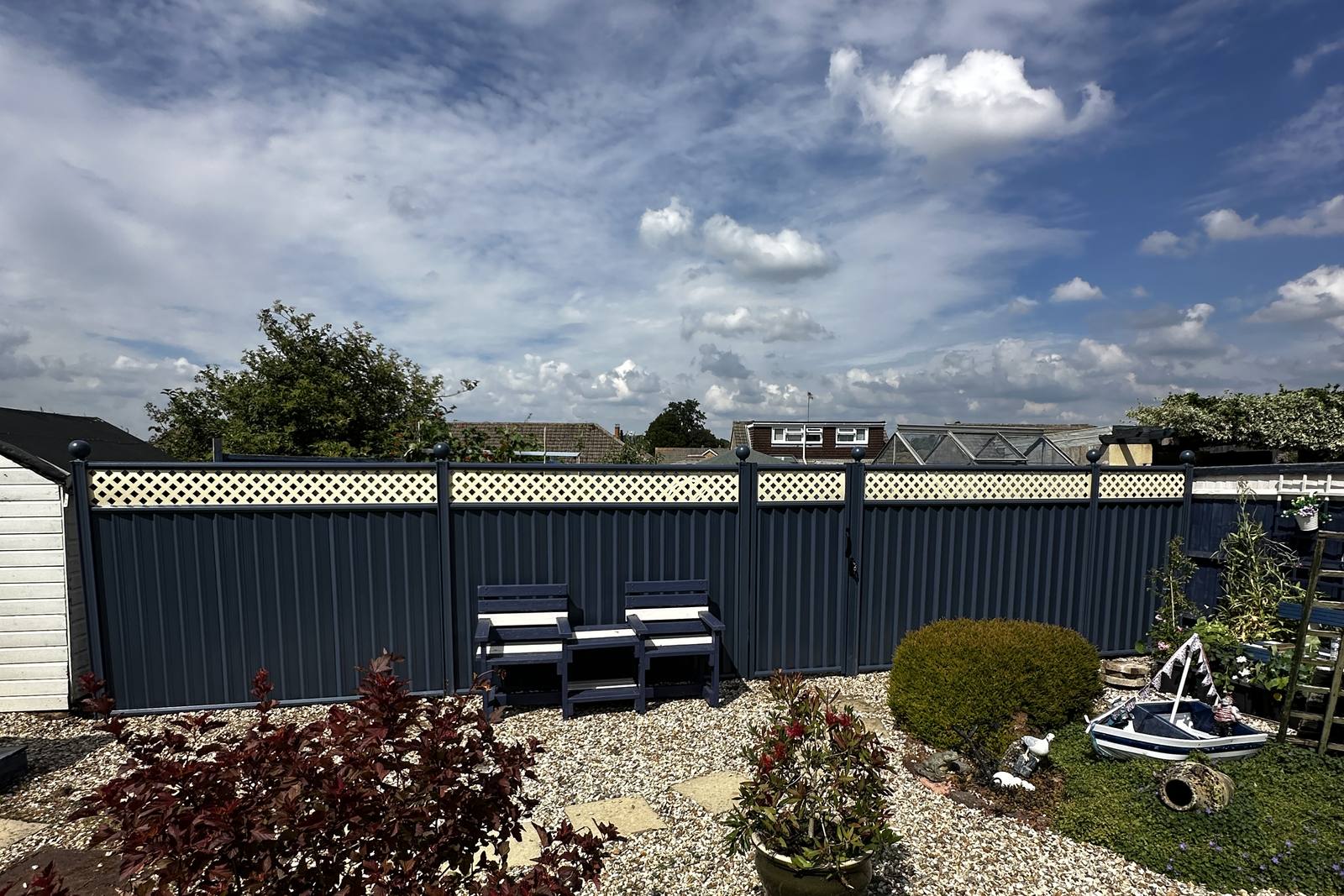 Blue metal fencing with cream decorative lattice in a landscaped garden.