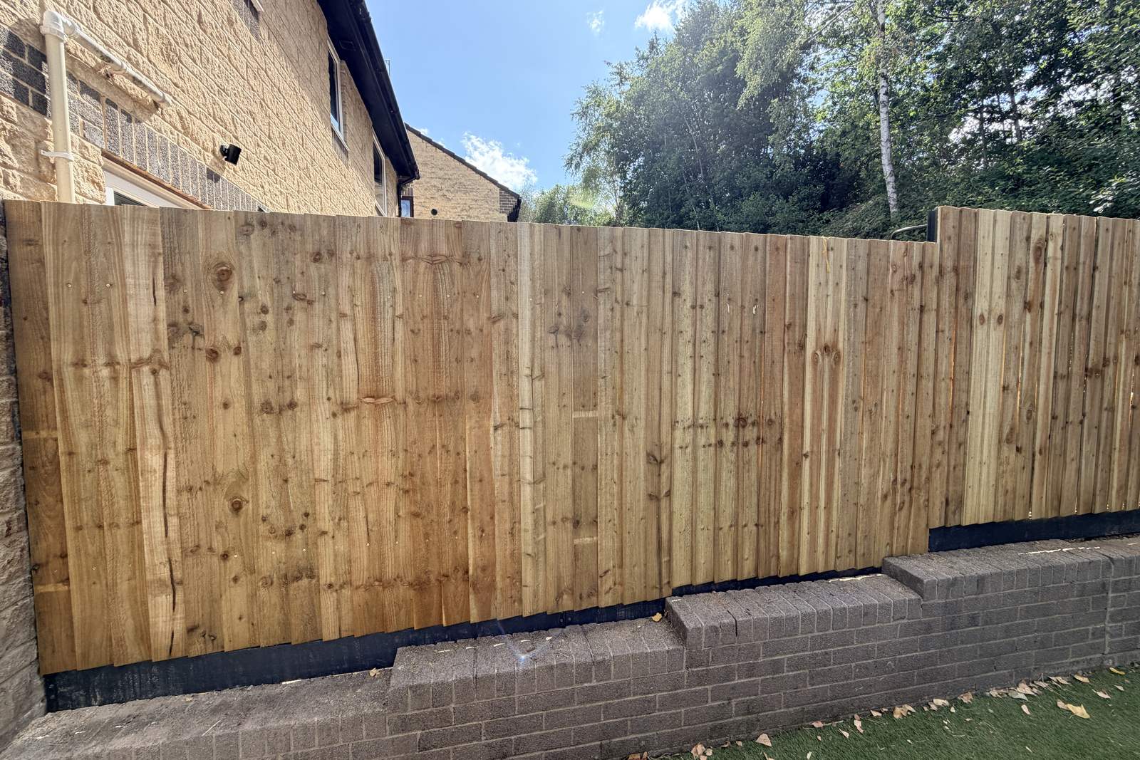 Closeboard timber fencing on a steel post system, above a brick wall.