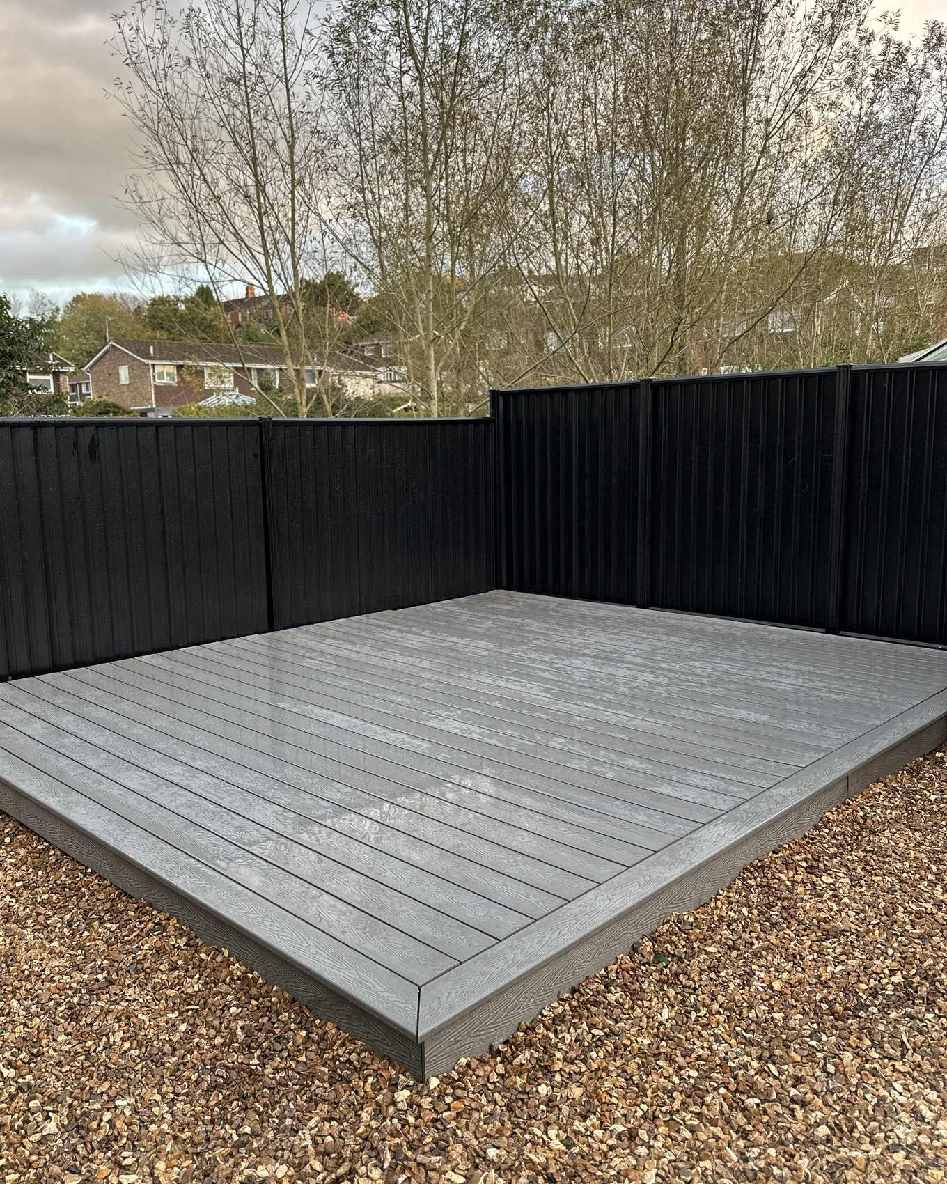 Grey composite decking in a garden with black boundary fencing.