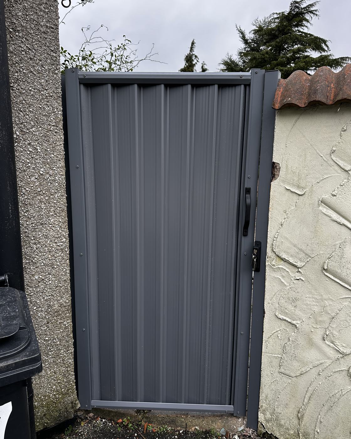 Grey pedestrian gate between garden boundaries.